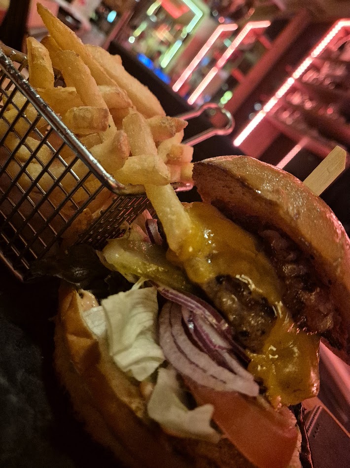 Diner-artiger Cheeseburger mit Pommes, roten Zwiebeln und Neonatmosphäre
